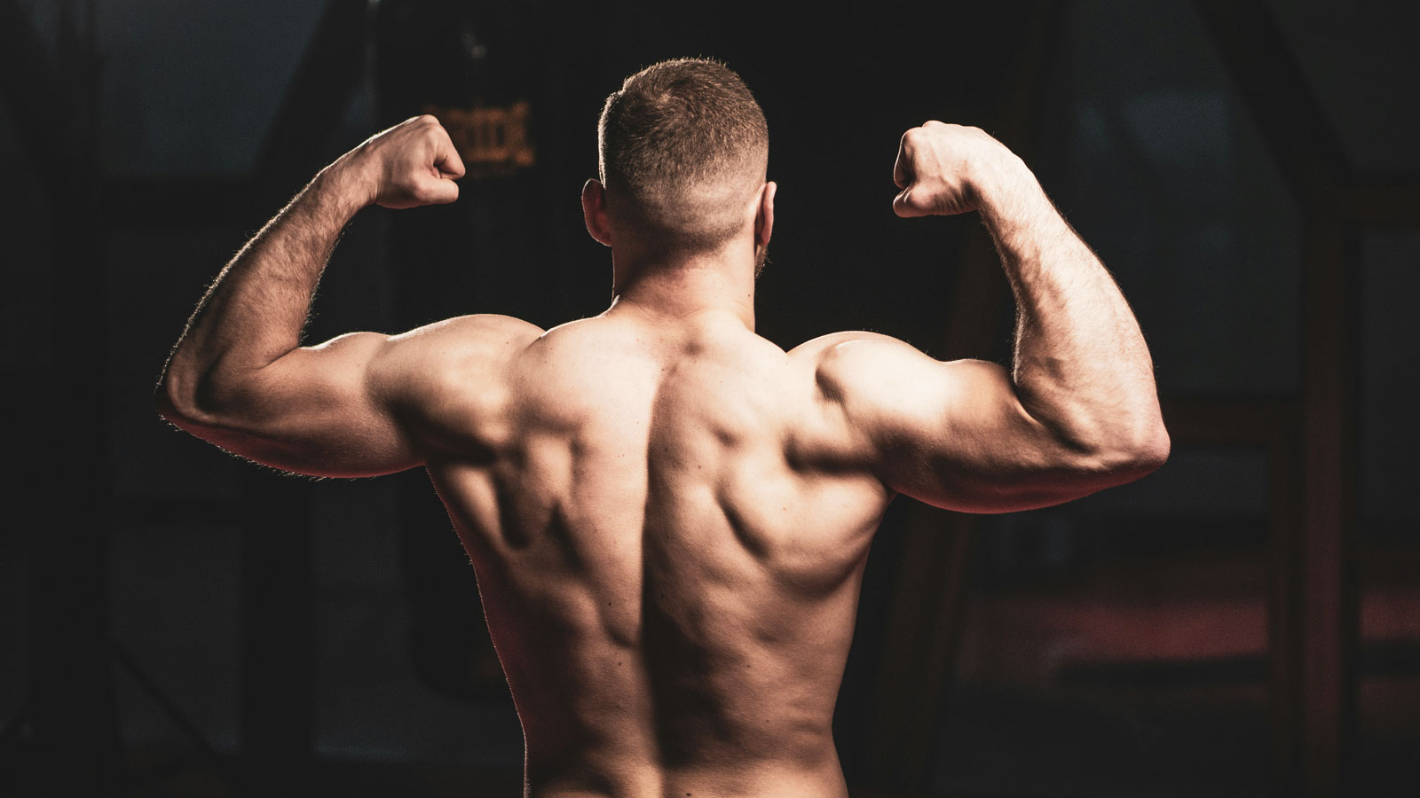 Man flexing his muscles inside a gym to display his muscular definition and progress from strength training