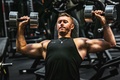 Man exercising with a dumbbell in each hand while resting his back and head against an adjustable gym bench inclined at approximately 45 degrees