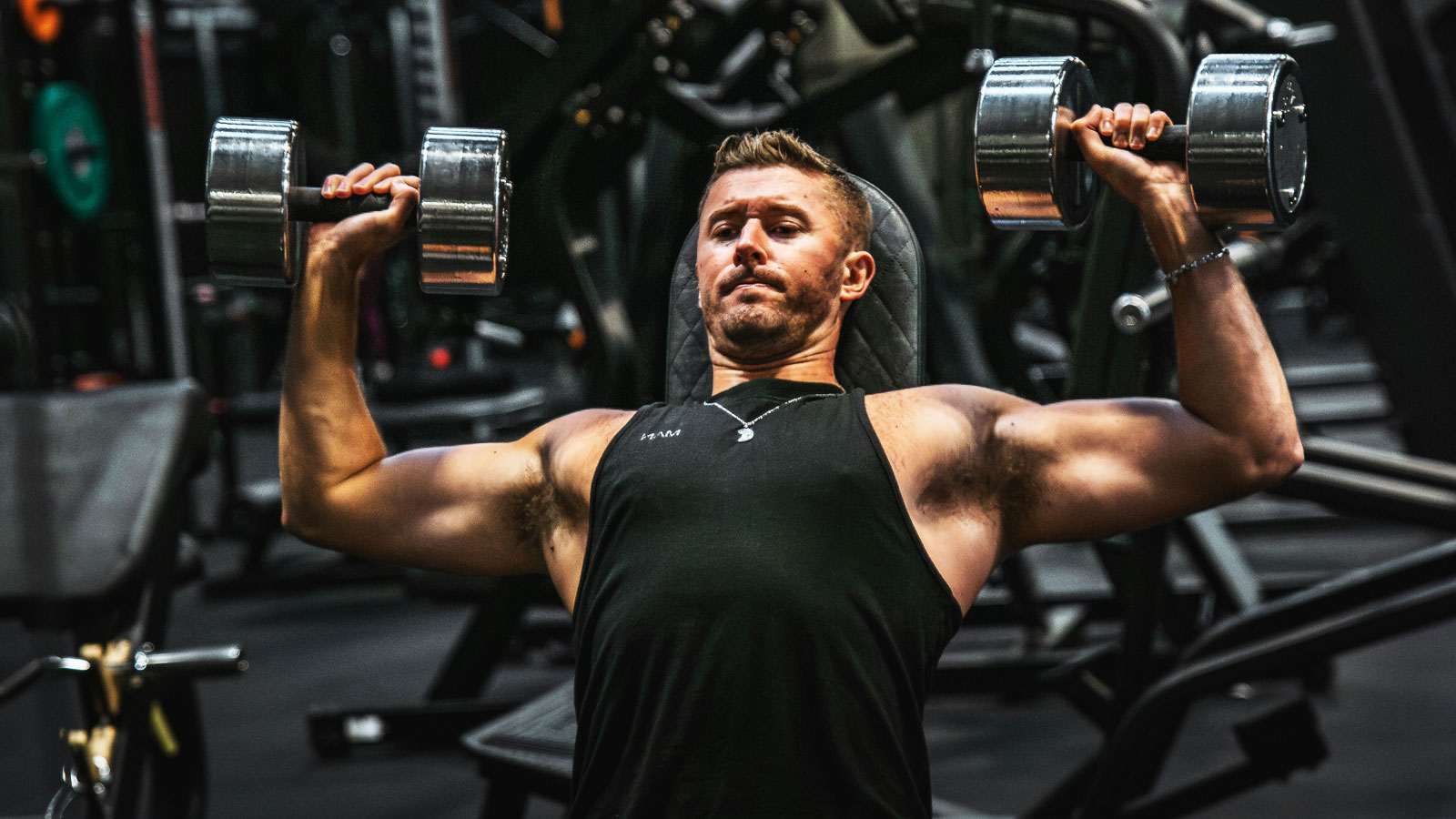 Man exercising with a dumbbell in each hand while resting his back and head against an adjustable gym bench inclined at approximately 45 degrees