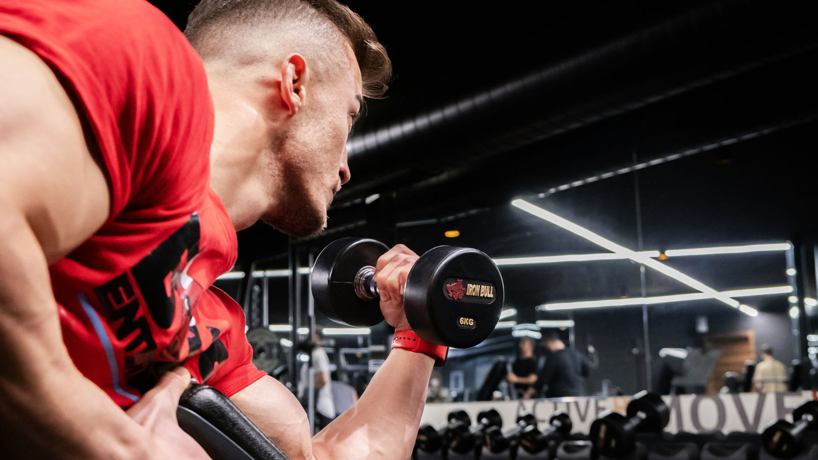Man exercising in a gym while lifting a dumbbell with one arm to perform a biceps curl
