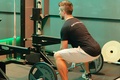 Man positioned in a squat near a gym bench preparing to lift weights while maintaining a controlled exercise posture