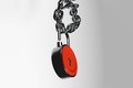 Metal padlock hanging from a heavy chrome chain with interlocking links against a pale grey background