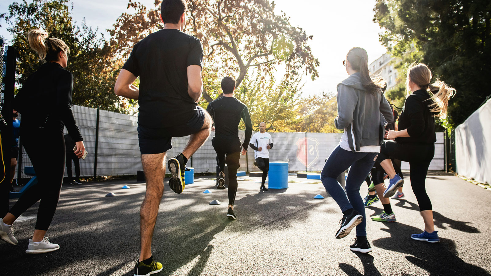 Group of people exercising on an outdoor paved surface while following an instructor demonstrating leg movements during a fitness warm-up