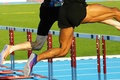 Two male athletes jumping over hurdles during a competitive track and field race while demonstrating speed, agility, and coordination