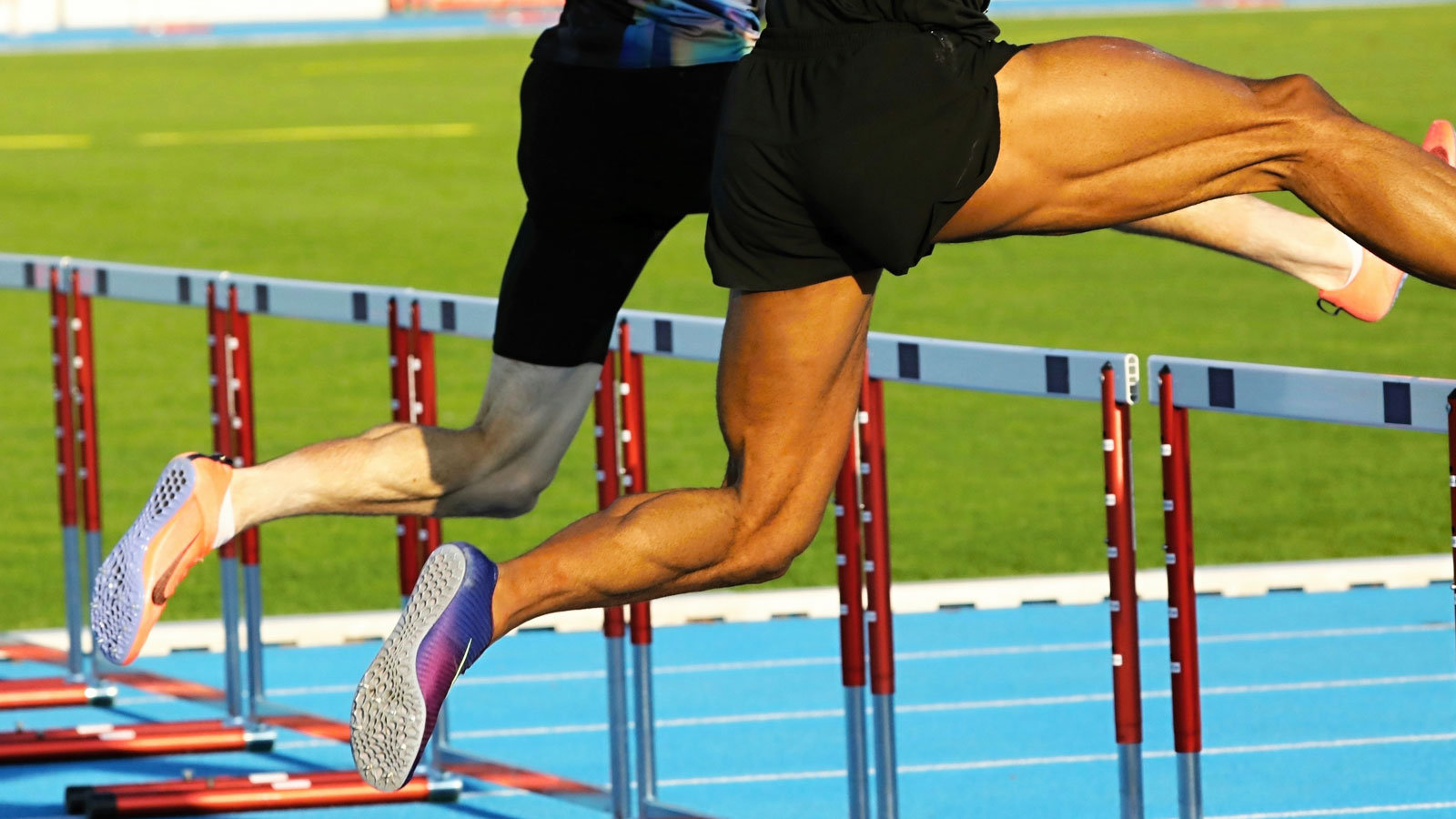 Two male athletes jumping over hurdles during a competitive track and field race while demonstrating speed, agility, and coordination