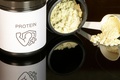 Container of vanilla-flavored protein powder with a measuring scoop arranged against a black background for a fitness nutrition setup