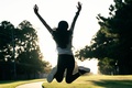 Woman photographed from behind jumping into the air with her arms raised and legs bent backward in an expression of happiness and excitement
