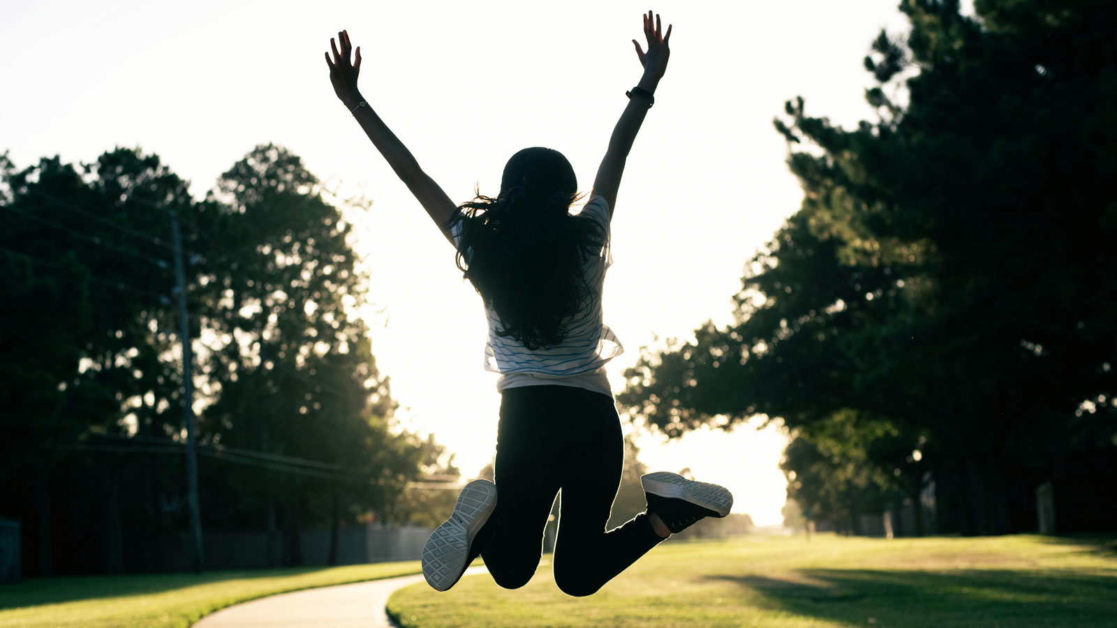 Woman photographed from behind jumping into the air with her arms raised and legs bent backward in an expression of happiness and excitement