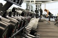Woman standing inside a gym surrounded by exercise equipment and weights of different sizes for progressive strength training