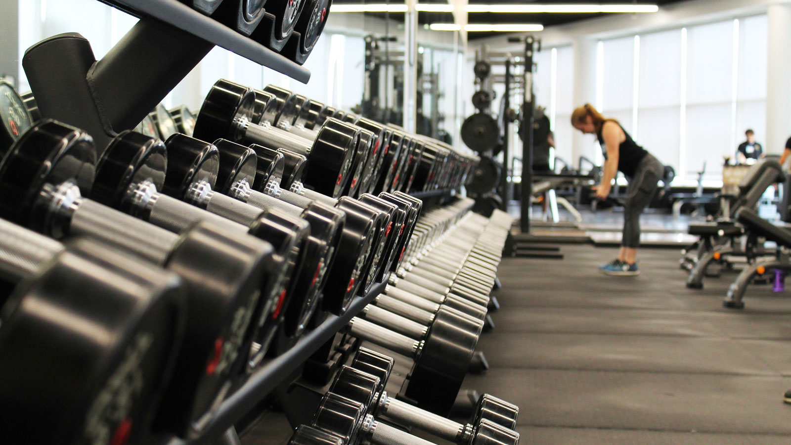 Woman standing inside a gym surrounded by exercise equipment and weights of different sizes for progressive strength training